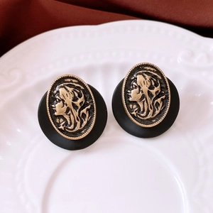 Macro detail of French vintage black and gold cameo resin stud earrings on a white plate