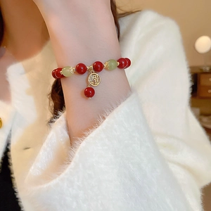 Détail du bracelet en agate rouge et jade avec pendentif Fu doré au poignet