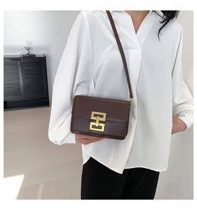 Brown leather crossbody bag with golden H-buckle worn by model in white shirt