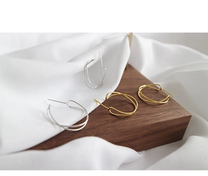 Detail of minimalist gold and silver twisted hoop earrings on wooden blocks and white silk