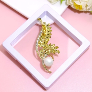 Close-up of golden leaf brooch with yellow stones and white pearl in a display box