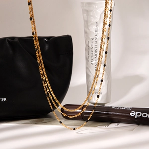 Detailed view of layered gold necklace with black beads draped on a black leather bag