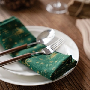 Serviette de Noël vert foncé avec rennes dorés et flocons de neige sur une assiette