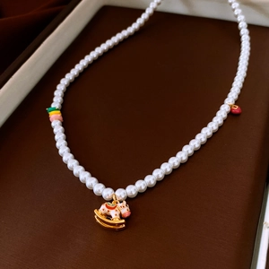 Détail macro d'un collier de perles avec un pendentif cheval à bascule en émail et breloques