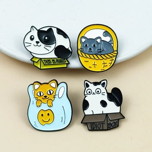 Set of four cute cartoon cat enamel pins in boxes and baskets on a beige table
