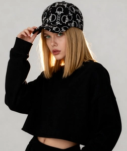 Side view of a black baseball cap with white monogram patterns and a cropped sweatshirt