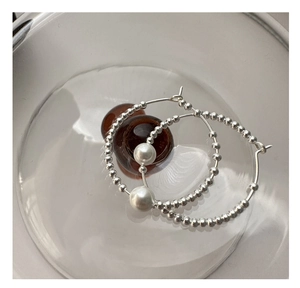 Close-up of S925 sterling silver beaded hoop earrings with white pearls on a glass plate
