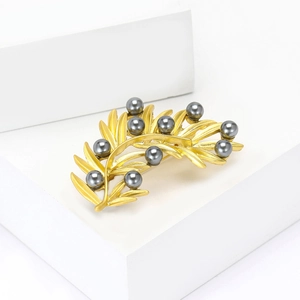 Elegant gold leaf brooch with gray pearls on a white geometric display stand