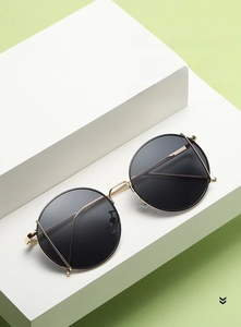 Elegant round gold metal sunglasses for women with black gradient lenses on a green backdrop