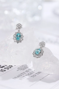Detail of sunflower-style silver earrings with oval light blue gemstones and white zircons