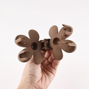 Detail view of flower-shaped brown matte hair claw clip showing internal teeth and spring