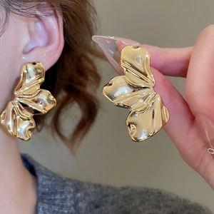 Detail showing oversized golden wave metal earrings held to demonstrate scale and texture