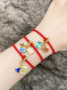 Dettaglio di tre braccialetti in corda rossa con ciondoli a tema viaggio dorati e smalto