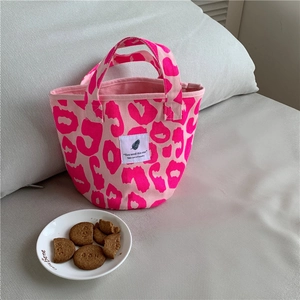 Detailed close-up of pink leopard print canvas tote bag with woven label on sofa