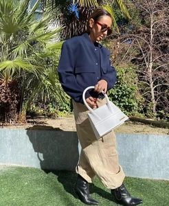 Dettaglio di una borsa a mano in pelle bianca con logo metallico portata da una modella