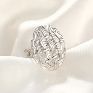 Close-up of a silver hammered ring with a woven hollow pattern on white silk fabric