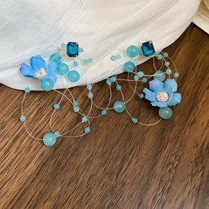 Close-up of blue fabric flower earrings with navy glass stones on a textured backdrop