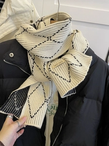 Detail of beige knit scarf with black diamond pattern and handmade woven label
