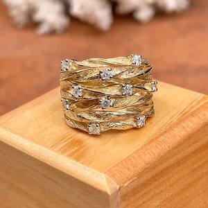Golden multi-strand vine ring with cubic zirconia stones on a light wood block