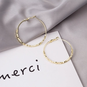 Detailed view of gold round hoop earrings with square bead charms on silk background