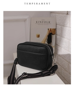 Detail of black lychee grain PU leather crossbody bag with striped wide shoulder strap