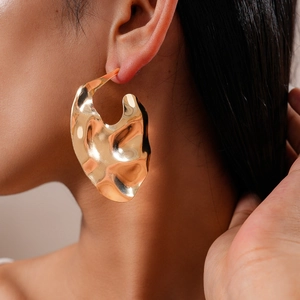 Gros plan d'une boucle d'oreille en métal doré au design ondulé irrégulier sur un mannequin