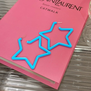 Detail view of vibrant blue star acrylic earrings on a pink decorative catwalk book