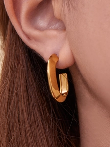 Detailed close-up of polished golden oval hoop earring worn on an ear for size perspective
