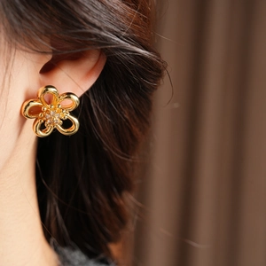 Detailed close-up of hollow flower stud earrings in gold with sparkling zircon inlay