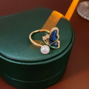 Detail of gold butterfly ring with blue shell inlay, zircon stones and white pearl