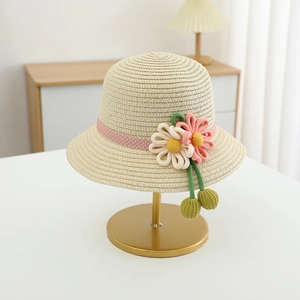 Detail of girls beige straw hat with pink polka dot ribbon and woven flowers on a stand