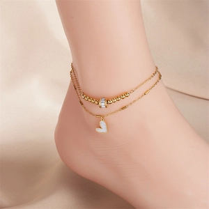 Double-layered gold anklet with heart pendant and zircon beads shown on silk background