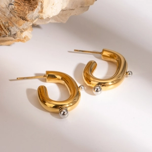 Detailed view of U-shaped gold earrings with silver beads on a natural rock background
