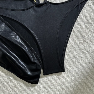 Détails d'un bas de bikini noir avec anneau en métal doré et tissu extensible brillant