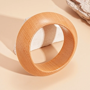 Detail of wide wooden bangle showing natural light yellow grain on a textured stone