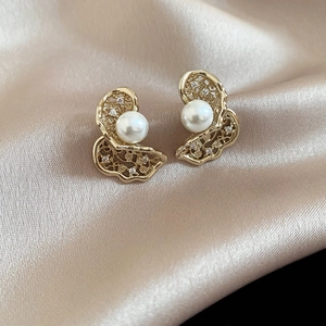 Macro shot of gold hollow pearl earrings with micro-diamonds on champagne silk fabric
