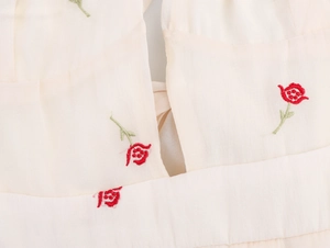 Close-up of red flower embroidery and textured fabric on a cream halter dress