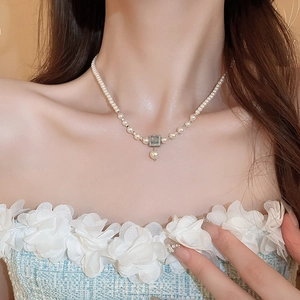 Detailed view of elegant pearl necklace with square pendant on woman's neck