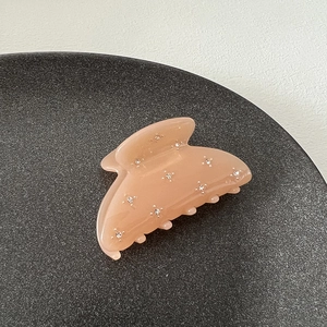 Close-up of translucent peach hair claw clip with rhinestones on a minimalist gray tray