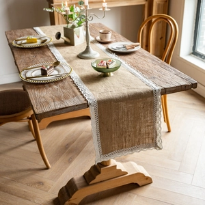 Detail of natural jute table runner featuring white lace borders on a wooden table setup