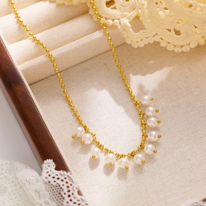 Detailed view of a gold bead chain necklace with ten white pearls in a jewelry box