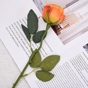 Artificial burnt orange rose on an open book page for home wedding photography decor