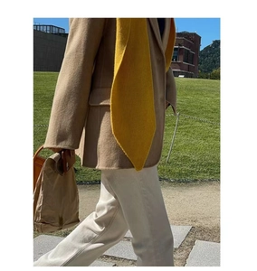 Close-up of a vibrant yellow knitted scarf paired with a camel wool blazer in a garden setting