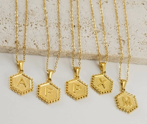 Detail showing five gold hexagonal letter pendants with beaded edges and matte texture