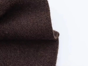 Détail macro de la texture douce en laine marron foncé sur la cape asymétrique en tricot