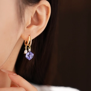 Close-up of gold earrings featuring purple cubic and clear teardrop zircon crystals on model