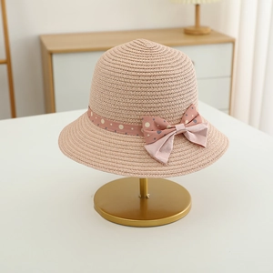 Detail of pink straw sun hat for girls with dotted bow decoration on a gold display stand