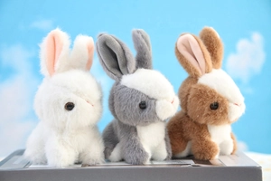 Three plush bunny keychains in white, grey, and brown sitting on a book outdoors