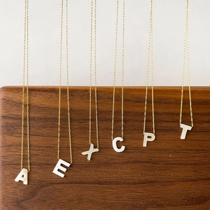 Colliers dorés minimalistes avec pendentifs lettres en nacre sur support en bois