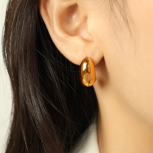 Polished gold titanium steel oval hoop earrings worn by a model for a stylish look